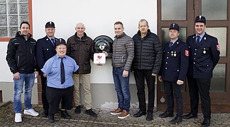 Vertreter der Feuerwehr Amerbach mit den Sponsoren vor dem neuen Defibrillator am Feuerwehrhaus. Personen im Bild von links nach rechts: Rainer Fackler, Michael Hönle, Sebastian Holzner, Konrad Mayer, Klaus Hönle, Josef Fackler, Michael Schneid, Daniel Trollmann