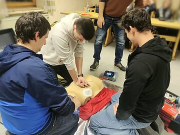 Praktische Anwendung der Ersten Hilfe Eine Gruppe von Teilnehmern bei der praktischen Durchführung der Reanimation bestehend aus Herzdruckmassage, Beatmung sowie Anbringen und Nutzung des Defis.
