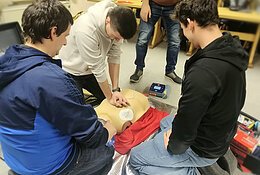 Eine Gruppe von Teilnehmern bei der praktischen Durchführung der Reanimation bestehend aus Herzdruckmassage, Beatmung sowie Anbringen und Nutzung des Defis.