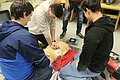Eine Gruppe von Teilnehmern bei der praktischen Durchführung der Reanimation bestehend aus Herzdruckmassage, Beatmung sowie Anbringen und Nutzung des Defis.
